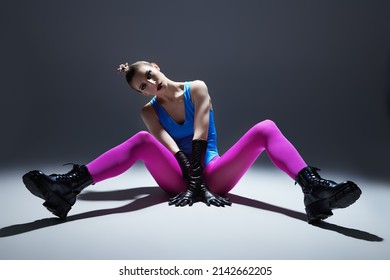 Modern vanguard fashion. A gorgeous model girl in bright extravagant clothes posing on the floor. Gray studio background. Black makeup.