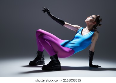 Modern vanguard fashion. A gorgeous model girl in bright extravagant clothes posing on the floor. Gray studio background. Black makeup.