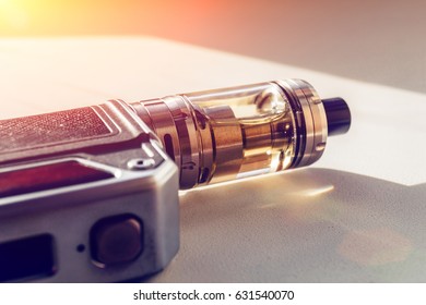 Modern vape device: electric box mod on dna chip and tank with vaping liquid in sun light