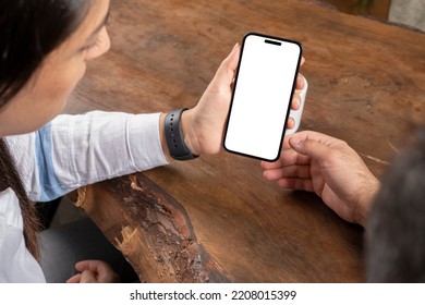 Modern Vertical Smartphone Mock Up, Over Shoulder View Of Modern Vertical Smartphone Mock Up. Couple Sitting On Wooden Table, Looking White Blank Screen Of Mobile Phone. Video Call, Recommend Concept.