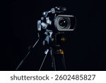 Modern video camera with tripod on black background