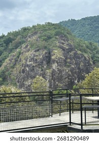 Modern viewing platform with a table and chairs overlooking lush green mountains under a cloudy sky