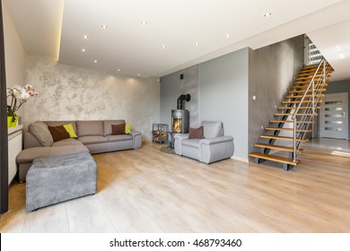 Modern villa interior with extra large sofa, fireplace in industrial style, wood floor panels, decorative wall finish and wooden stairs