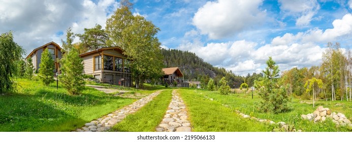 Modern village. Real estate in ecologically clean place. Panorama with rural town houses. Wooden cottages at foot hill. Summer landscape ECO village. Stone path leads to summer houses. ECO property