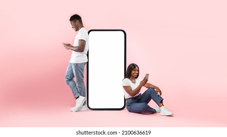 Modern Virtual Communication. Creative Collage Of Young Black Couple Leaning On Big Cell Phone Screen With Blank White Screen For Mock Up Template, Guy And Lady Chatting, Sending And Reading Sms