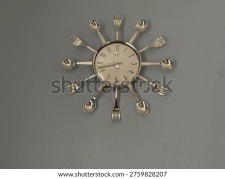 Modern wall clock made of stainless steel spoons and forks on grey background