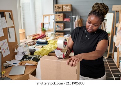 Modern warehouse worker sealing cardboard box with cellotape by workplace