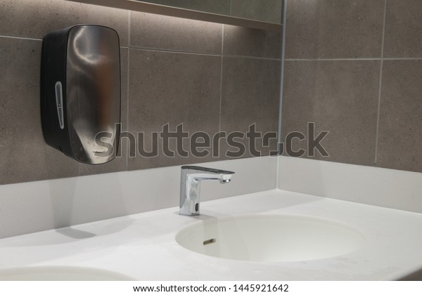 Modern wash hand\
basin with hand free sensor tap and soap dispenser. Solid Surface\
worktop and grey tiled\
wall.