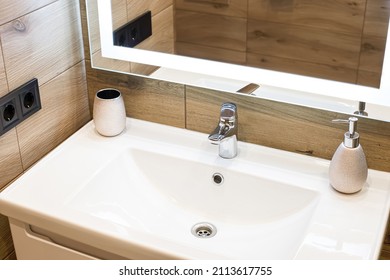 Modern washbasin with chrome faucet beside a stylish soap dispenser. Mirror with built-in led lighting. - Shutterstock ID 2113617755