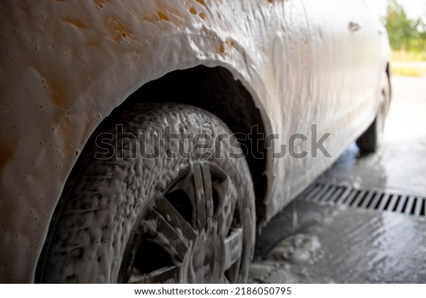 Modern washing with foam and high-pressure\
water of a white car. Foam on the car.\
