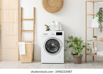 Modern washing machine with basket, shelving unit and ladder near white wall. Interior of home laundry room