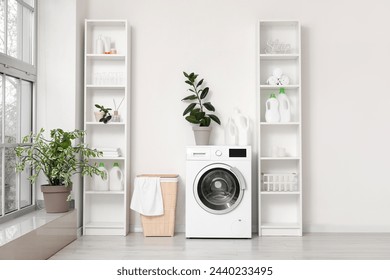 Modern washing machine with basket and shelving units near white wall. Interior of home laundry room