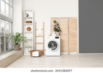 Modern washing machine with basket, shelving unit and dressing screen near white wall. Interior of home laundry room - Powered by Shutterstock