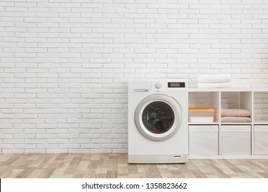 Modern washing machine near brick wall in laundry room interior, space for text
