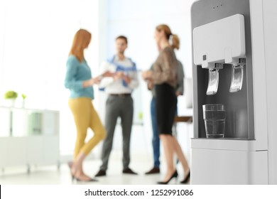 Modern water cooler with glass and blurred office employees on background. Space for text - Powered by Shutterstock