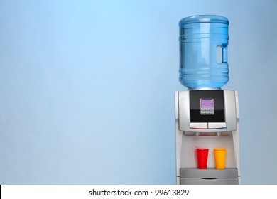 Modern Water Cooler On Blue Background With Red And Yellow Plastic Cups