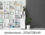 Modern water cooler with paper cups and shelf unit in office