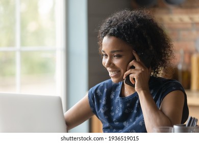 Modern way of communication. Smiling biracial female hold cell at ear talk look at pc screen. Busy young black lady advisor lawyer give phone consultation from home discuss electronic document details - Powered by Shutterstock