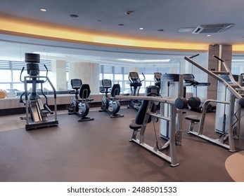 A modern, well-equipped gym with a row of treadmills and elliptical machines lined up in front of large mirrors. The gym features a clean, minimalist design with ample lighting and a spacious layout.  - Powered by Shutterstock