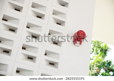 A modern white building wall with a repeating geometric pattern and a bright red fire hydrant mounted on the surface, set against a background of greenery and outdoor environment.