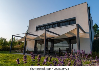 Modern, white, cube, elegant, minimalist style passive house with large panoramic windows, grey shutters in maintained garden. Wooden terrace. Sunny day. Lavender in front. - Shutterstock ID 2098736923