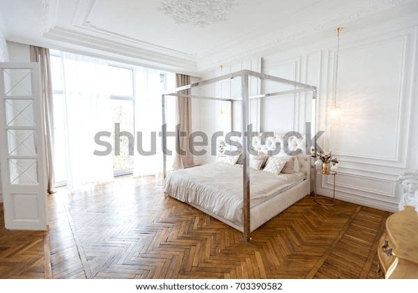 Modern white design interior in\
classical style of a spacious studio apartment with a huge\
four-poster bed, a wooden large shelf and a beautiful white\
sofa