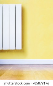Modern white electric heater mounted on a yellow wall in a room with wooden floor and white baseboard.