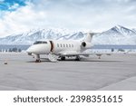 Modern white executive jet plane with an opened gangway door at the winter airport apron on the background of high scenic snow capped mountains