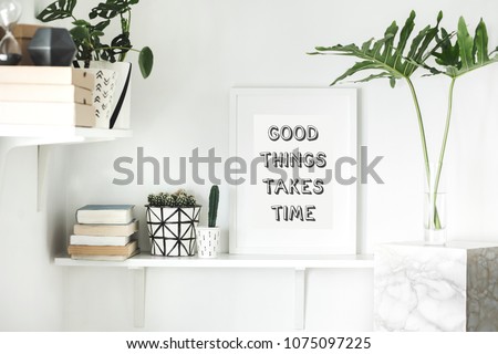 The modern white interior with cacti, tropical leaf, books, boxes, plant and mock up photo frame. Concept of scandi stylish room.