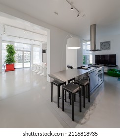 Modern white interior of spacious private house. Kitchen and dinner room. Table and chairs.