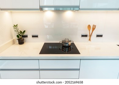 Modern white kitchen with granite countertops and white cabinet. Have modern black induction hob, cooker, Stainless steel slim line cooker hood 60cm. in kitchen. White tone and clean kitchen