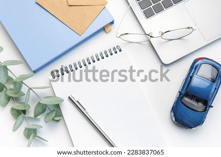 Modern white office desk table with laptop, notebook, toy car and other supplies. Blank copy space for  the text. Top view, flat lay. Concept of selling contracts, car dealerships offer