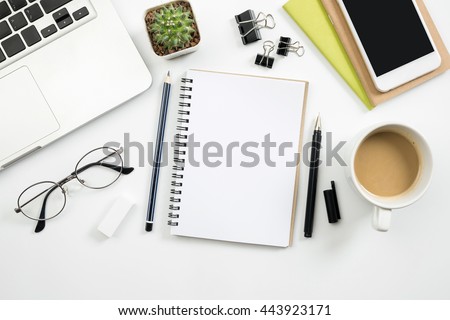Modern white office desk table with laptop, smartphone and other supplies with cup of coffee. Blank notebook page for input the text in the middle. Top view, flat lay.