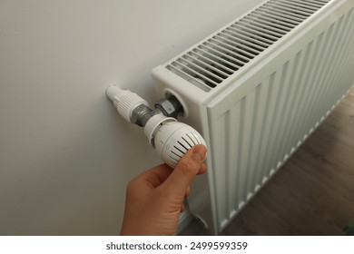 Modern white radiator with thermostat reduced to economy mode, Woman adjusting thermostat on white heating radiator