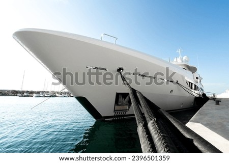Modern, white and spotless superyacht at dock in a port in the Greeece, Mediterranean sea, with black fenders, dock lines and a sunny day 