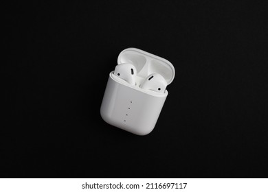 Modern white wireless earbuds headphones lying in a charging case on black background.