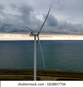 Modern Wind Turbine By The Sea At Sunset Generating Clean Energy.