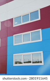 Modern windows in white plastic frames on the facade of a blue and burgundy industrial building.