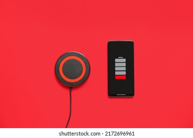 Modern Wireless Charger Pad And Uncharged Mobile Phone On Red Background