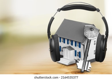 Modern Wireless Headphones On A Small House Against A Background. Home Soundproofing Concept.