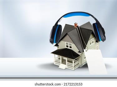 Modern Wireless Headphones On A Small House Against A Background. Home Soundproofing Concept.