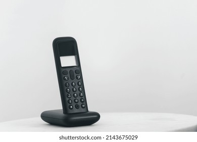 Modern Wireless Phone Handset On Black Cordless Station. Telephone With Empty Display And Keypad Standing On Table, Against White Copy Space Background. Communication And Telecommunication Concept