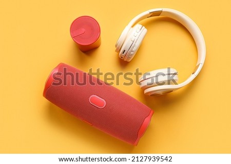 Modern wireless portable speakers and headphones on color background