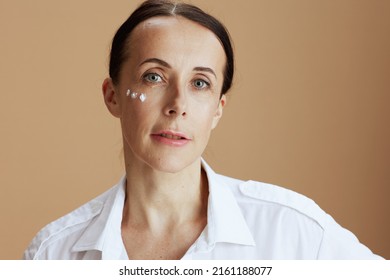 Modern Woman With Eye Cream On Face In White Shirt Isolated On Beige.