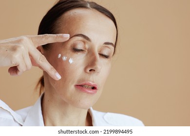 Modern Woman With Eye Cream On Face Isolated On Beige Background.