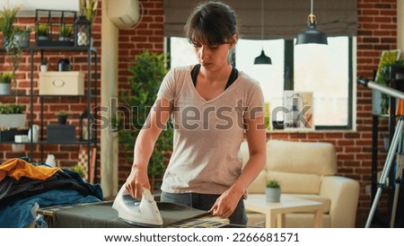 Modern woman ironing clothes at home after doing laundry, using heat and steam to iron clothing on board. Independent wife taking care of household chores, housework and hygiene.