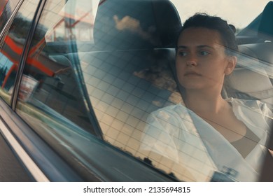 Modern Woman Sitting In Rear Seat Of Car On Road Trip Relaxing while watching the building's reflection view through the window.