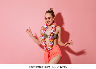 Modern Woman In Stylish Sunglasses, Cool Swimsuit, Pink Short Shorts And Necklace Of Flowers Smiling On Isolated Background..