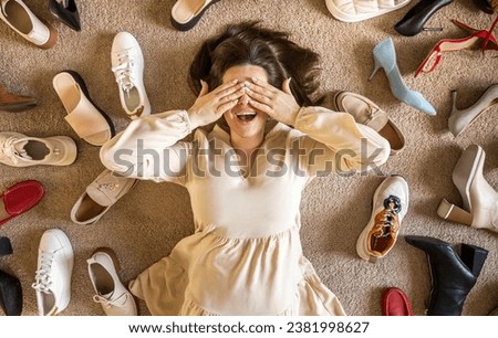 Modern woman surrounded by abstract shoes lying on beige carpet floor shopping consumerism top view. Female shopaholic with fashion vogue trendy footwear unreasonable consumption and abundance