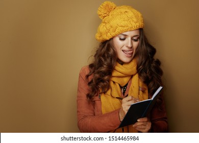 Modern Woman In Yellow Beret And Scarf Writing Goals In Notebook Against Beige Background.